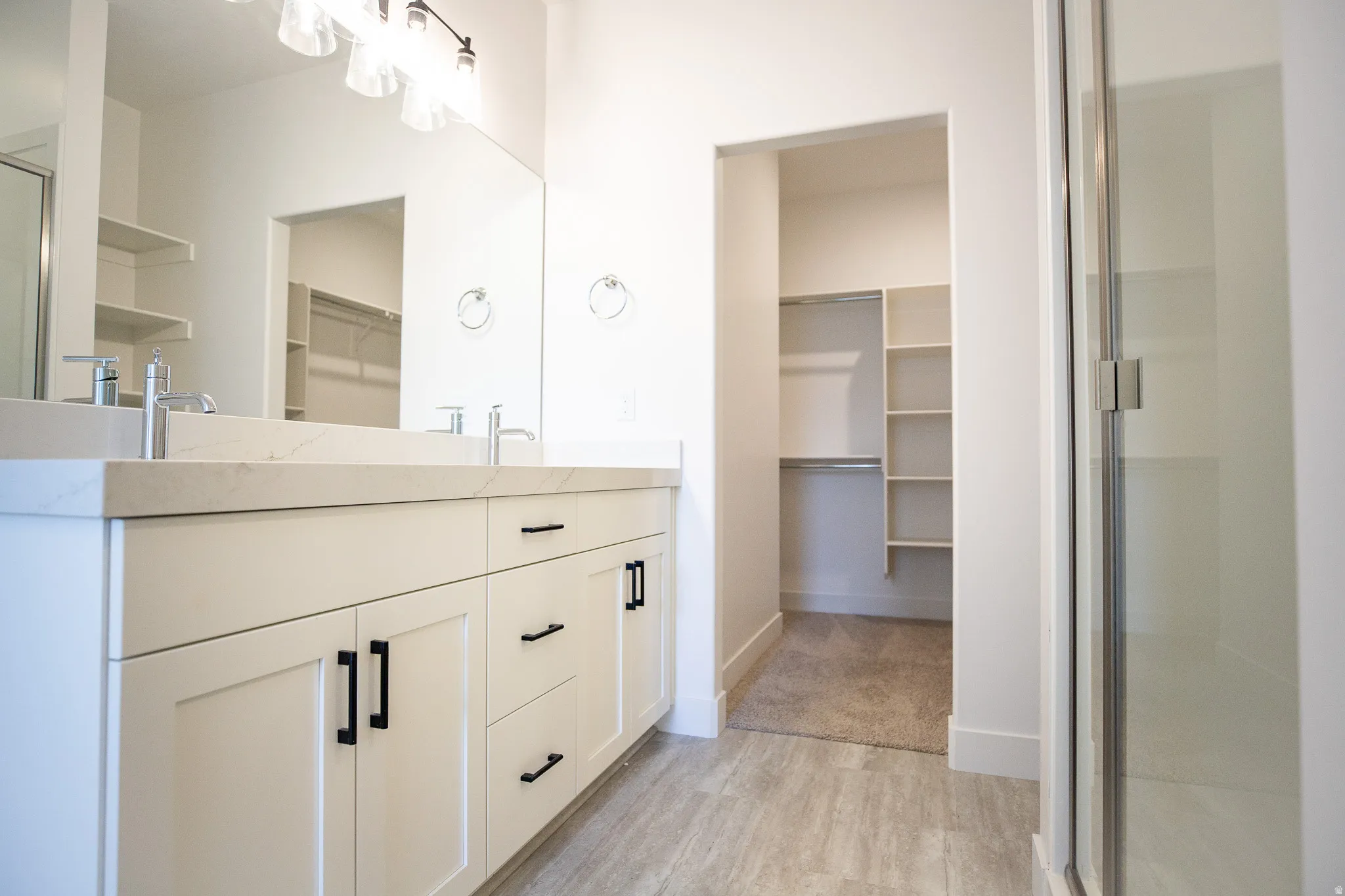 Primary bath with dual sinks, painted white wood cabinets, quartz slab countertops and spacious walk-in shower.