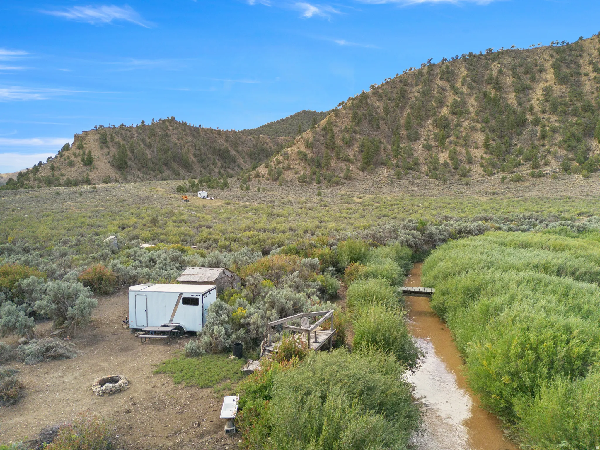 Expansive property featuring a natural water channel, wooden footbridge, and a fire pit