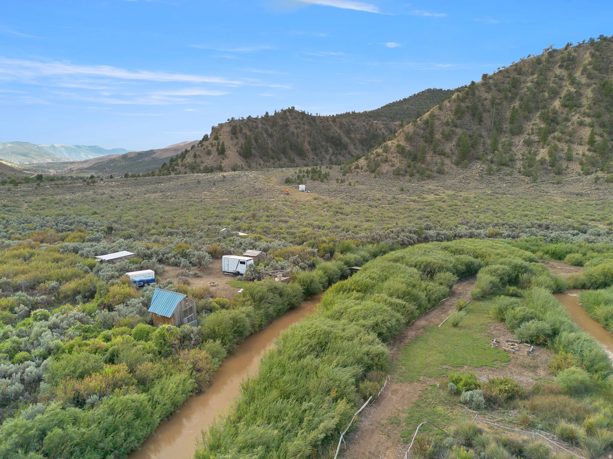 Expansive rural landscape featuring a winding river, mature vegetation, and distant mountains