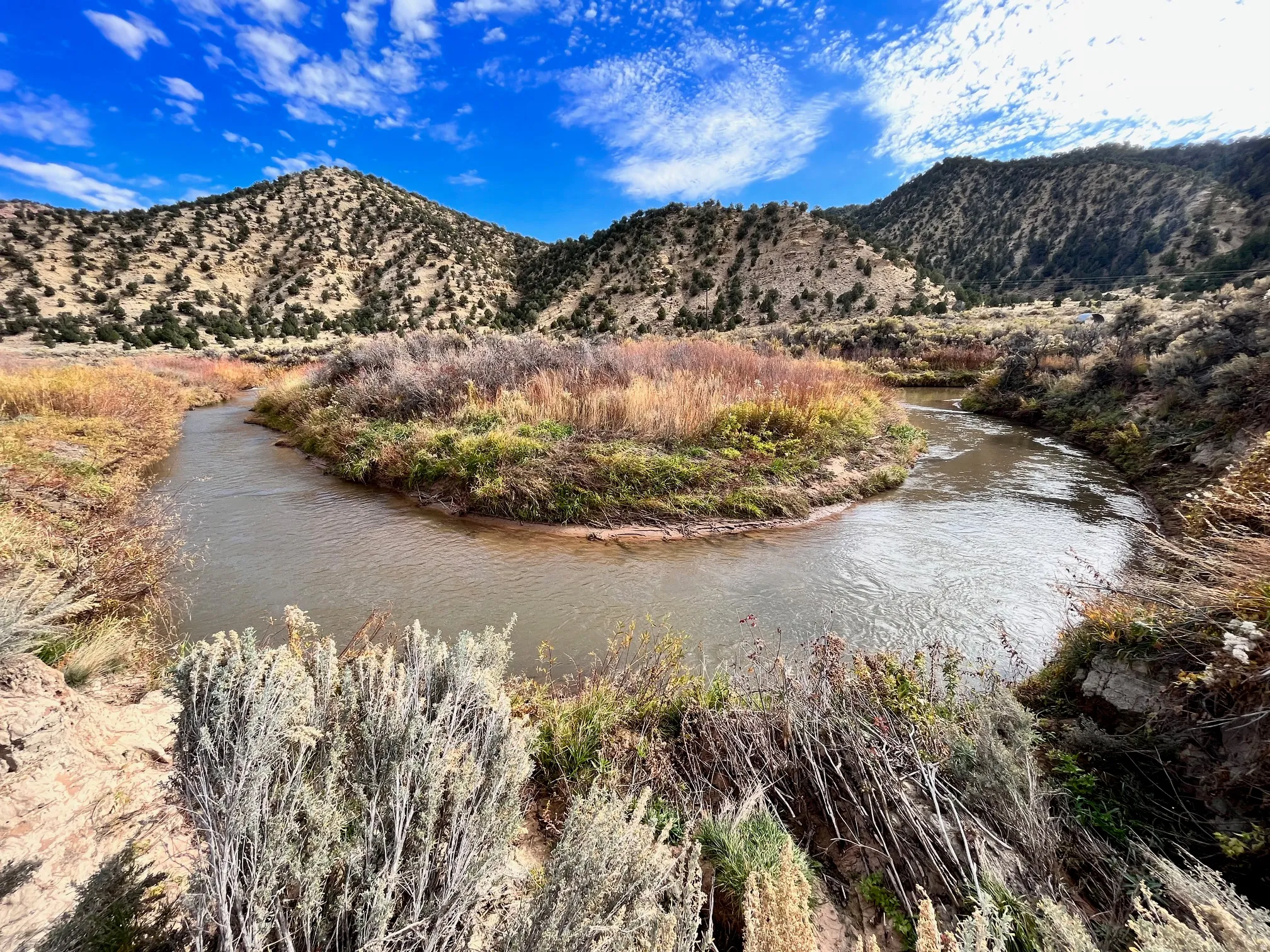 Winding river with natural banks, surrounded by varied native vegetation and distant hills