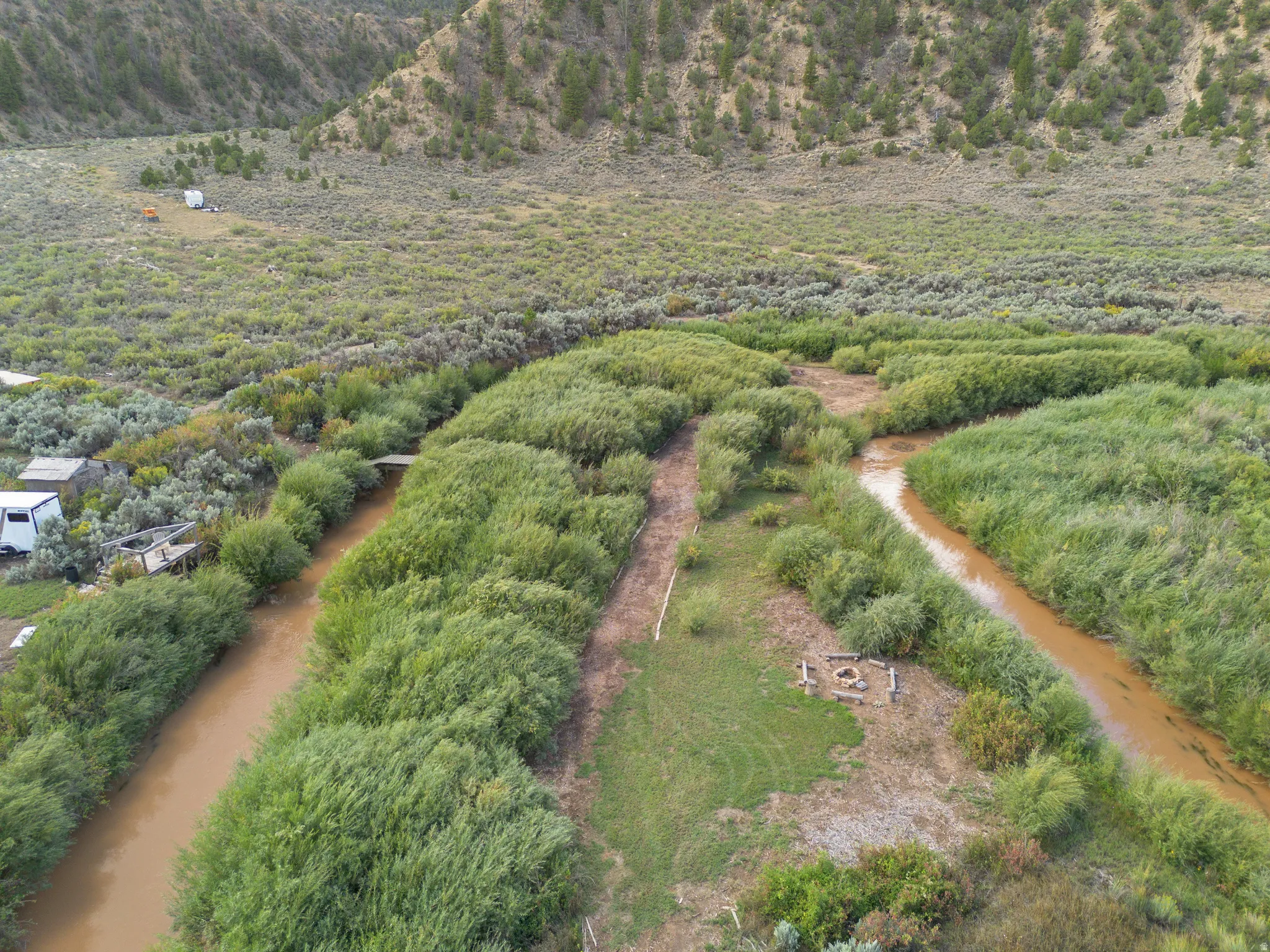 Natural landscape featuring a river, abundant greenery, and a fire pit area