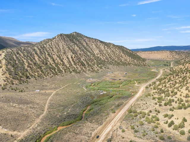 Expansive terrain with a winding dirt road, natural water feature, and distant structures nestled among hills