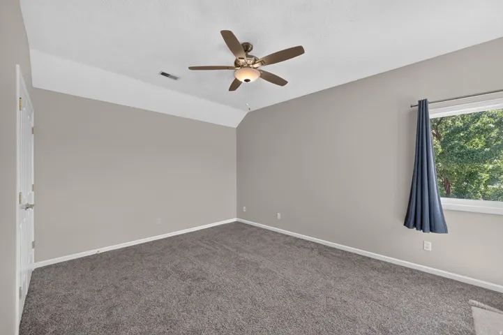 Carpeted room featuring a vaulted ceiling, ceiling fan with integrated lighting, and a window with exterior tree scenery