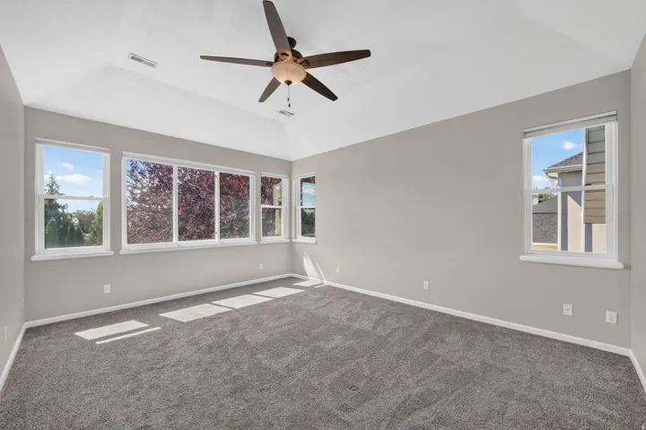 Vaulted ceiling with a ceiling fan, multiple windows with white trim, and neutral-toned carpeting