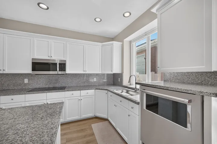 White shaker-style cabinetry, granite countertops, stainless steel appliances, undermount sink, and wood-finish flooring
