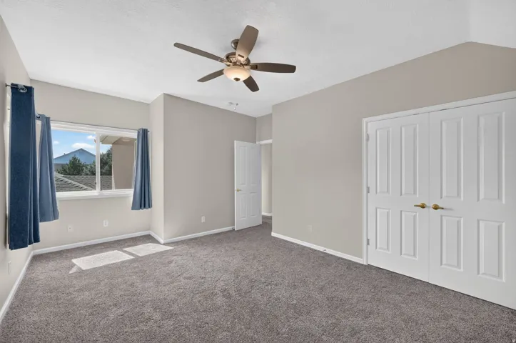 Carpeted room with a ceiling fan, a window showcasing distant mountains, and paneled bifold closet doors