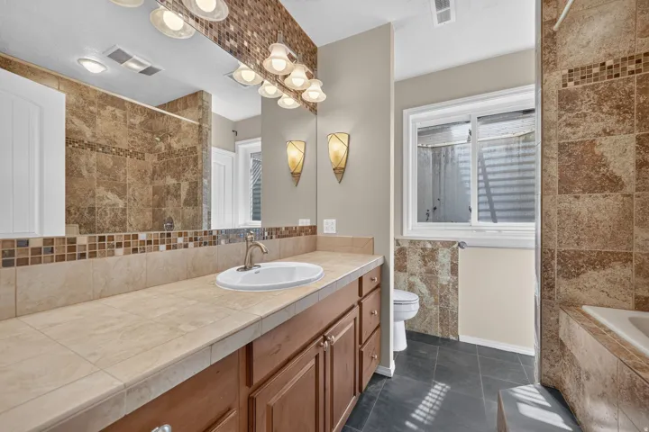 Extended vanity with tile countertop, integrated sink, and wood-finish cabinetry