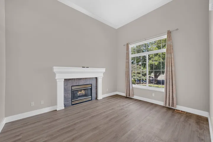 Vaulted ceilings with crown molding, a large picture window, wood-finish flooring, and a fireplace with a decorative mantel and tile surround