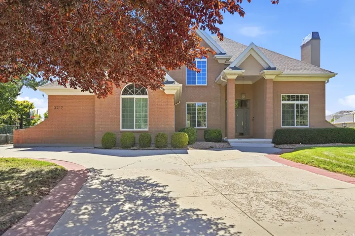 Brick-clad exterior with a prominent entry portico, multiple window styles including an arched window, a paved driveway, and manicured landscaping