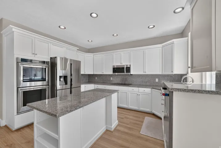 White cabinetry, stainless steel appliances, recessed lighting, wood-finish flooring, and a kitchen island with stone countertops
