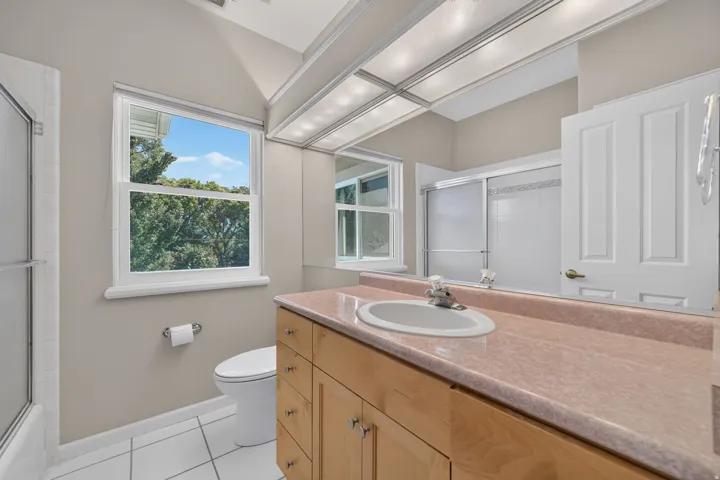 Bathroom featuring a wood-finish vanity with an integrated sink, a large wall mirror, and white tile flooring