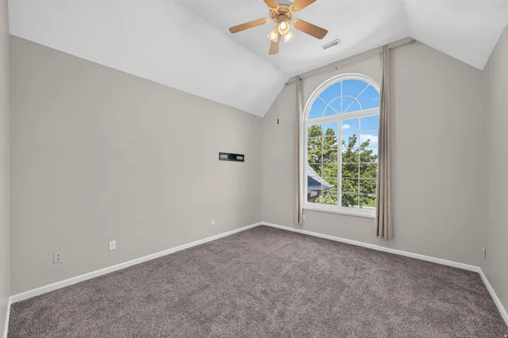 Vaulted ceiling with a ceiling fan, arched window, wall-to-wall carpeting, and neutral wall tones