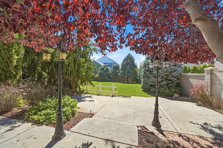 Mature tree with vibrant red foliage, concrete patio, ornamental lampposts, manicured lawn, and privacy fencing