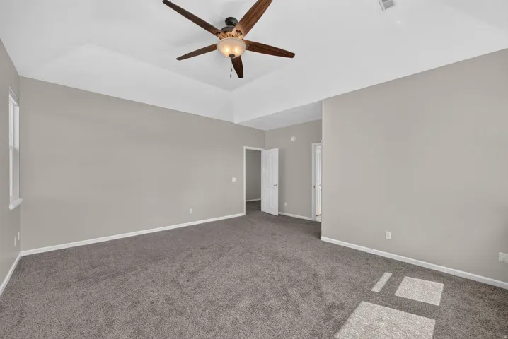 Tray ceiling, ceiling fan with integrated lighting, neutral wall paint, gray carpeting, and white trim