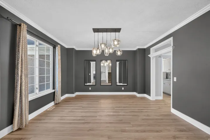 Spacious room with wood-finish flooring, dark gray walls, white crown molding, and a multi-bulb pendant light fixture