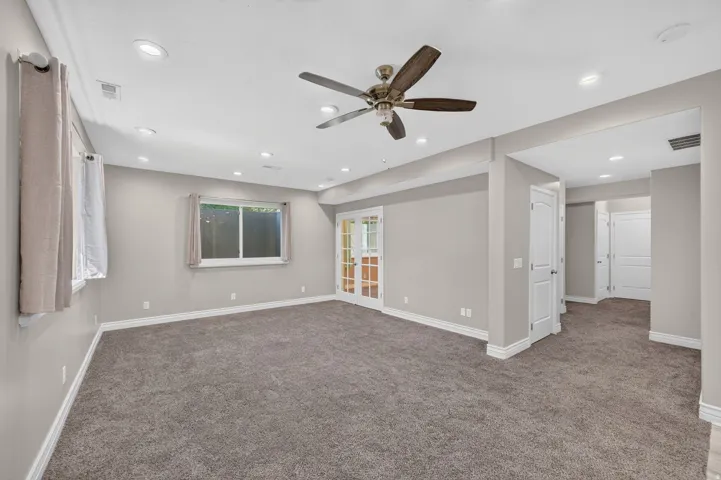 Spacious room featuring neutral carpeting, recessed lighting, a ceiling fan, and French doors