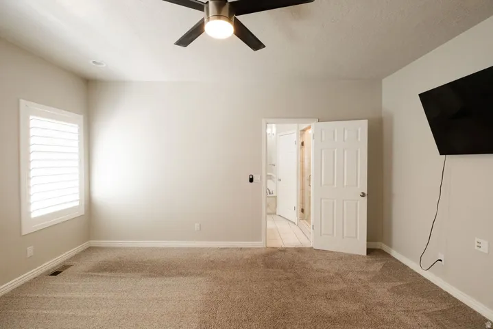 Carpeted room with a ceiling fan, plantation shutters, and a paneled door