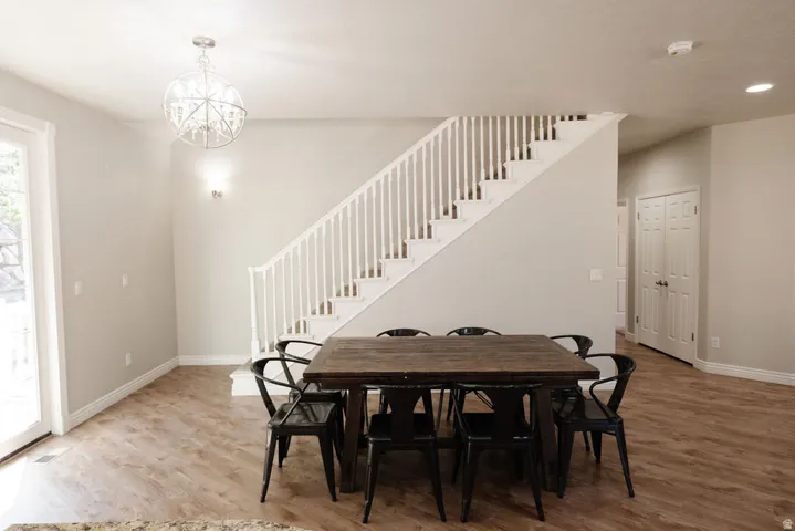 Open concept dining and living area featuring wood-finish flooring, a floating staircase with white spindle railing, and a crystal chandelier pendant fixture