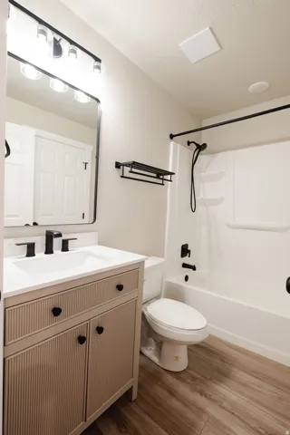 Modern bathroom featuring a vanity with integrated sink, sleek black fixtures, a white bathtub with shower, and wood-finish flooring
