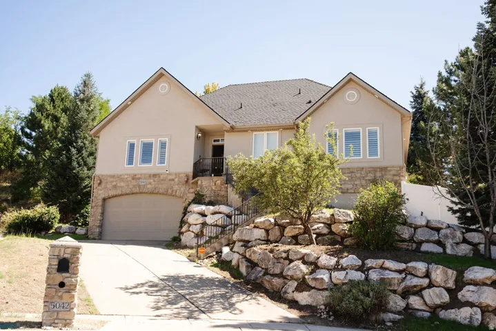 Stucco exterior with stone accents, arched garage door, stone retaining walls, and a stone mailbox pillar