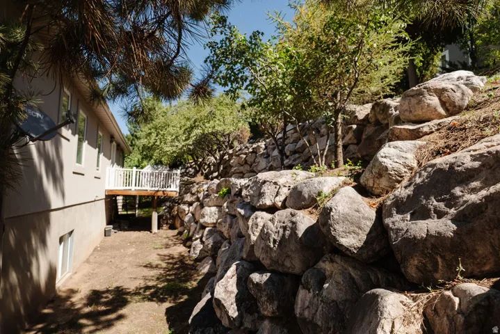 Exterior featuring a rock retaining wall, mature trees, and an elevated wood deck with white railings