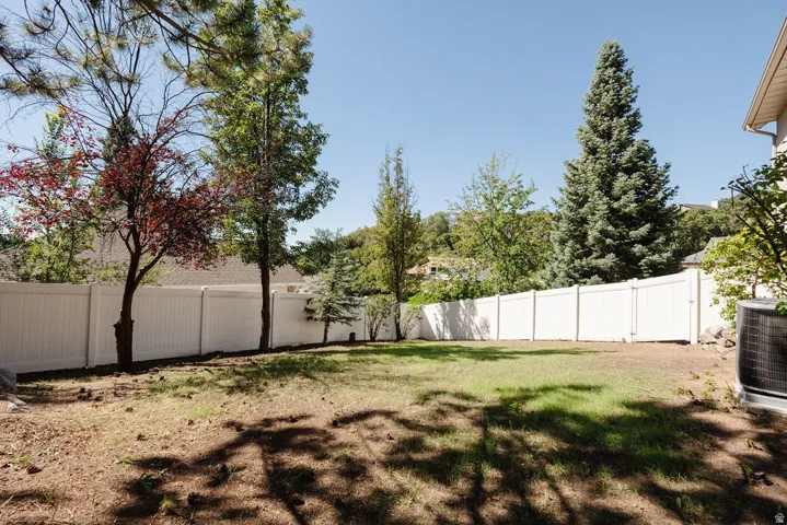 Expansive backyard with a white privacy fence, mature trees, and a partial lawn