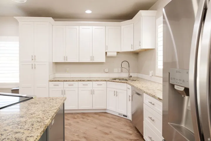 Kitchen featuring white shaker-style cabinetry, granite countertops, stainless steel appliances, and wood-finish flooring