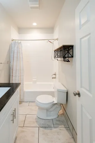 Subway tile shower surround with a white tub, dark stone countertop, white vanity cabinetry with brushed nickel hardware, and large format floor tile