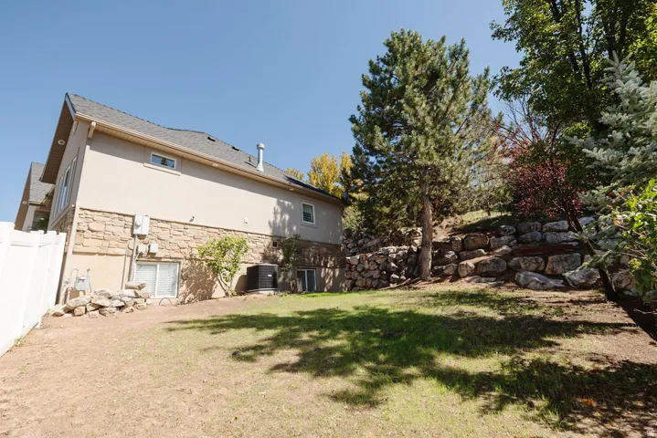 Expansive backyard featuring a stone retaining wall, mature trees, and a partial privacy fence
