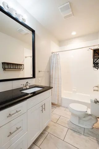 White vanity with brushed nickel hardware, black countertop, undermount sink, and large framed mirror