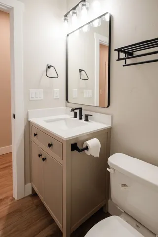 Bathroom featuring a vanity with an integrated sink, solid surface countertop, matte black fixtures, rectangular mirror, and wood-finish flooring