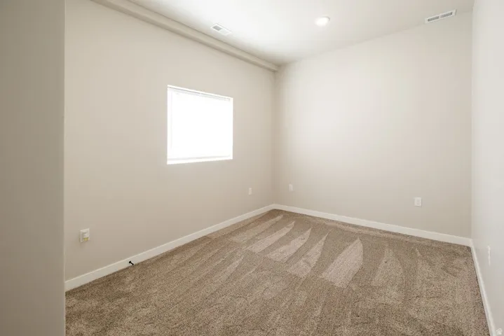 Neutral wall paint, plush carpet flooring, recessed ceiling lighting, and a single window with blinds