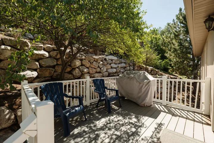 Outdoor decking area with white railing, stone retaining wall, and mature trees