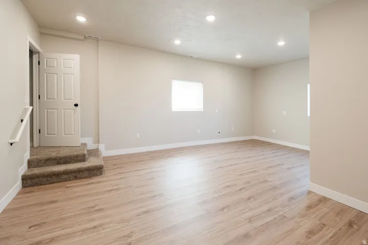 Recessed lighting, wood-finish flooring, two windows, two-step carpeted staircase, and white interior door