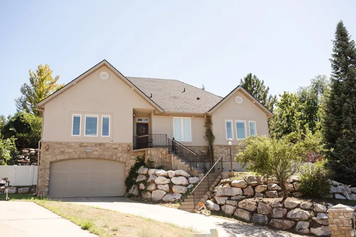 Stucco exterior with stone accent, arched garage entry, dark brown entry door, dark gray shingles, and decorative rock landscaping
