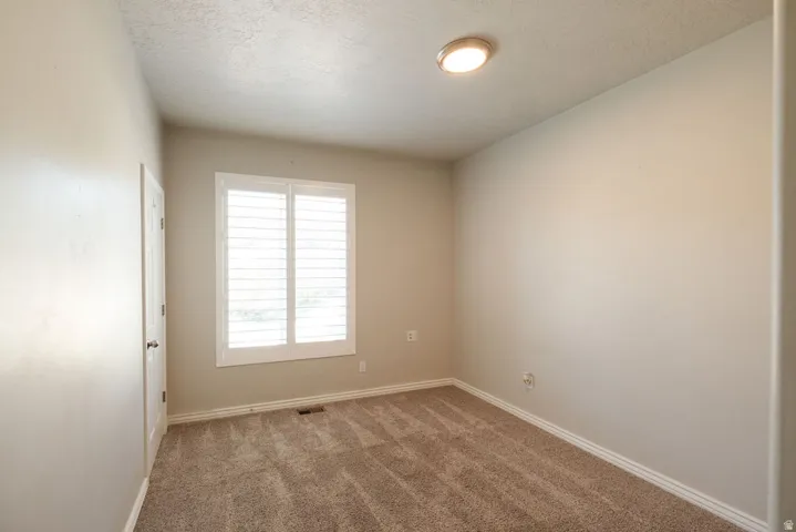 Neutral-toned walls, plush carpet flooring, window with white plantation shutters, and a flush-mount ceiling light fixture