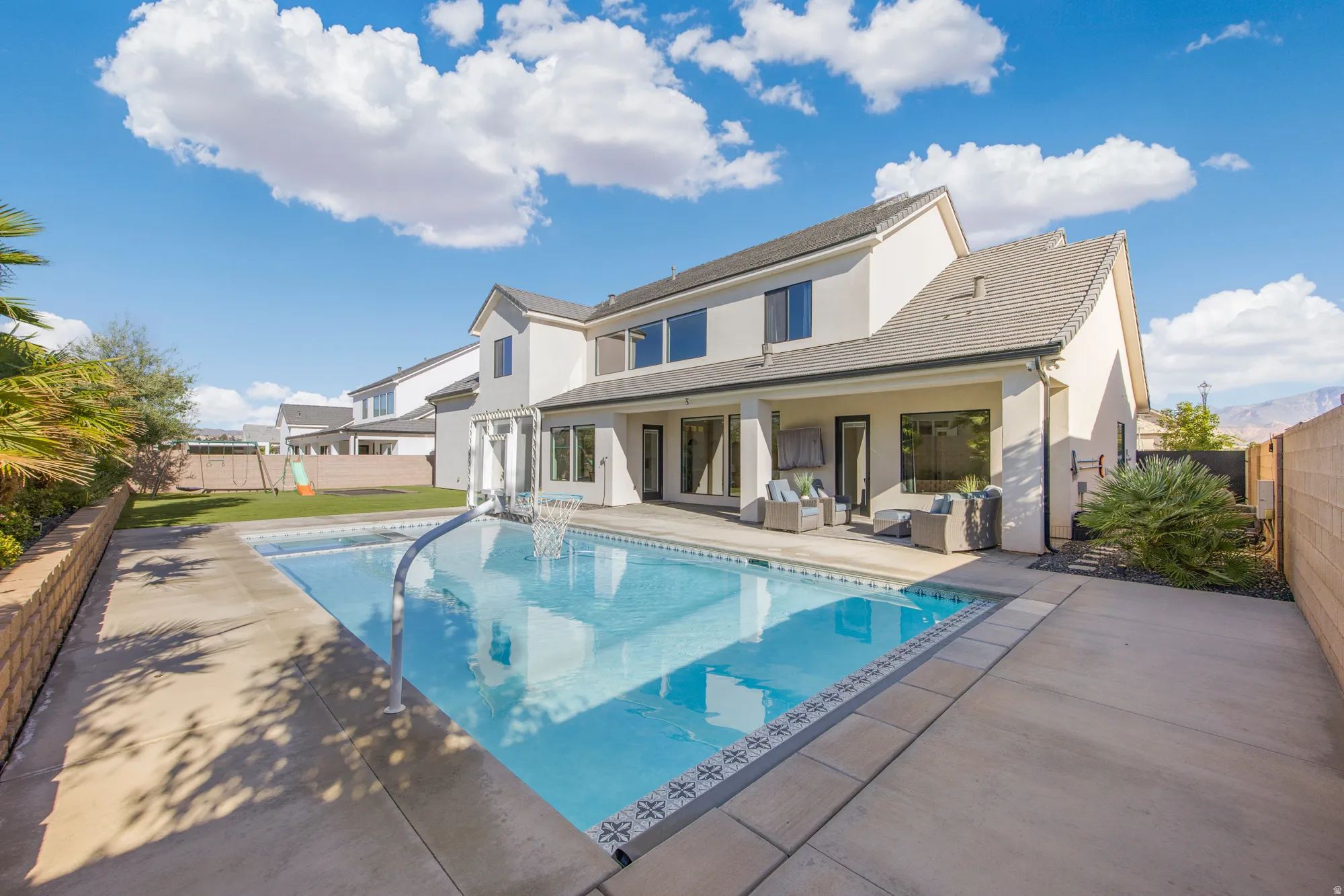 Expansive backyard featuring a swimming pool with integrated spa, concrete patio, covered patio area, mature landscaping, and stucco exterior