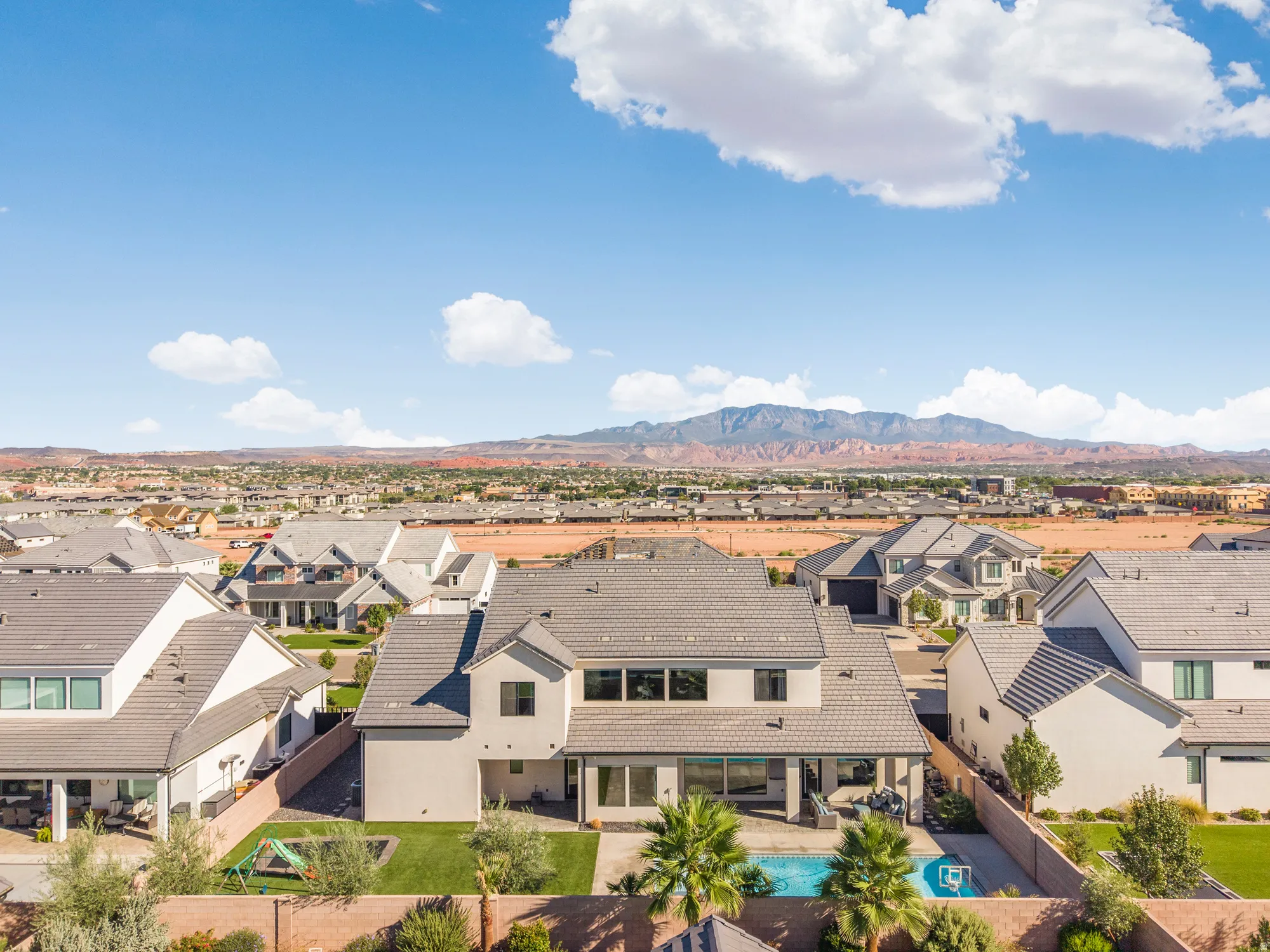 Modern stucco exterior with a tile roof, featuring a built-in swimming pool, a covered patio, and mature palm trees