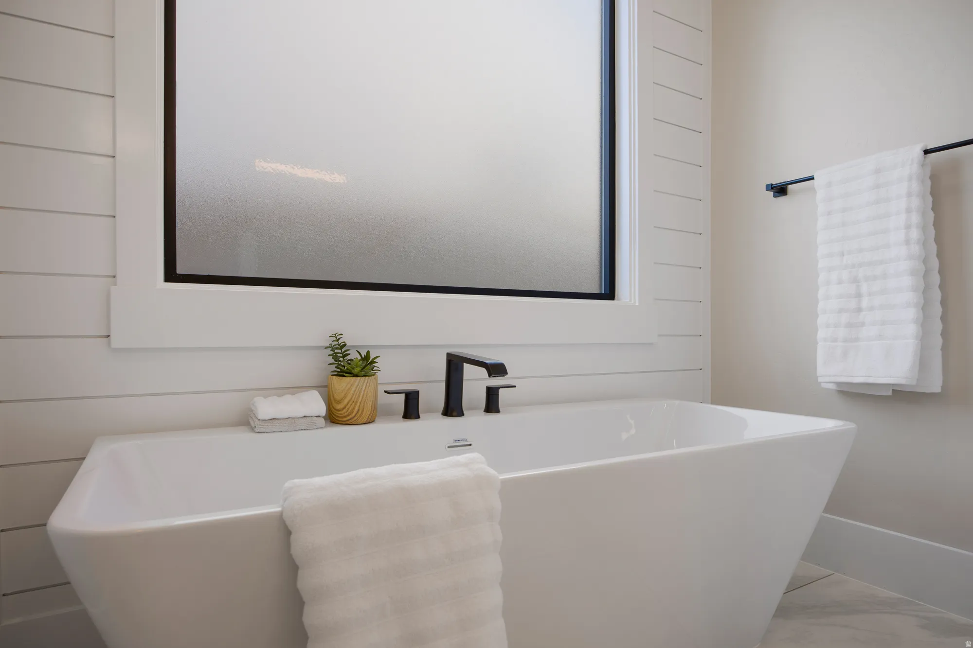 Freestanding soaking tub with matte black fixtures, shiplap accent wall, and a frosted glass window