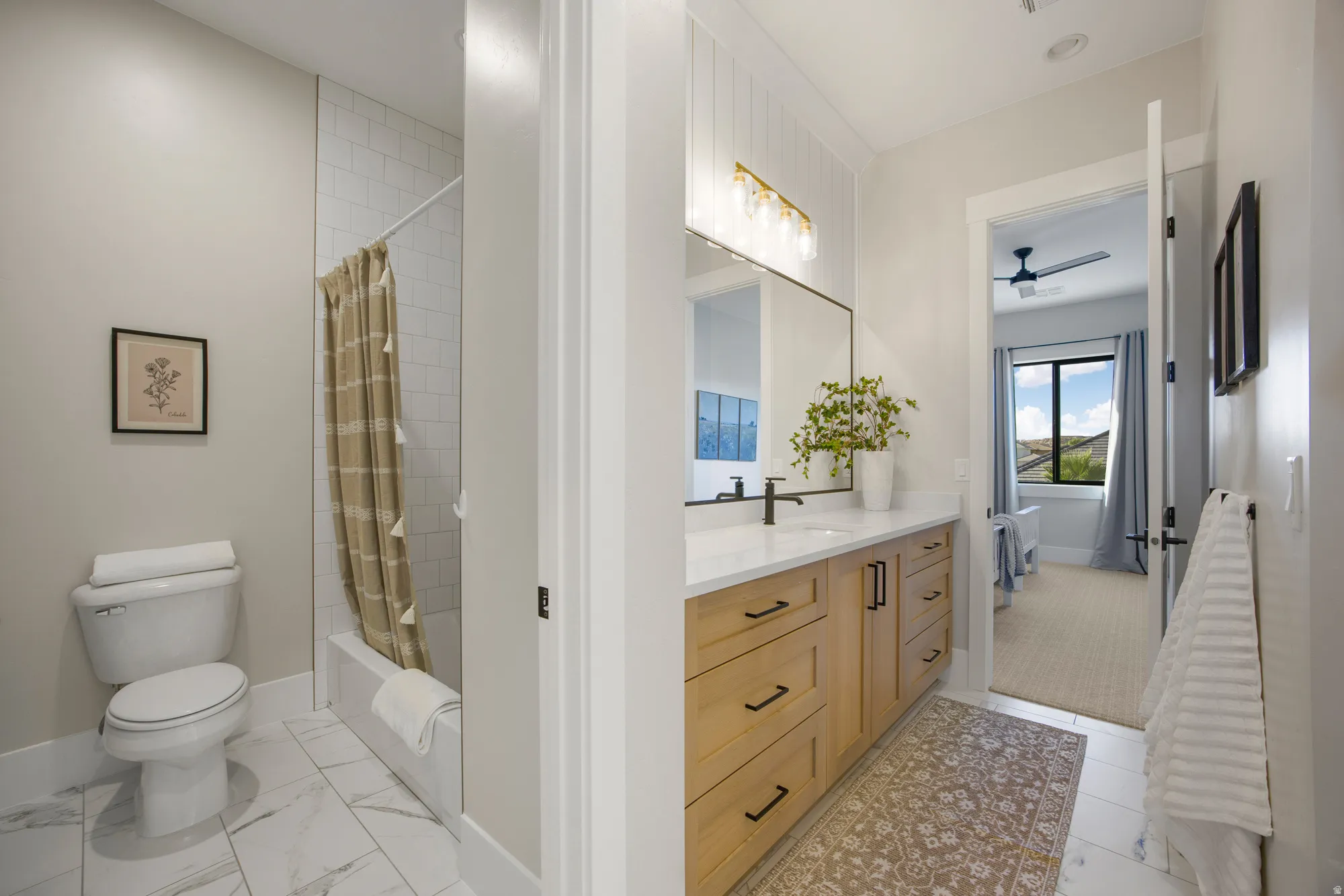 Bathroom featuring a light wood-finish vanity with a quartz countertop, a rectangular undermount sink with a matte black faucet, and a shower with subway tile surround