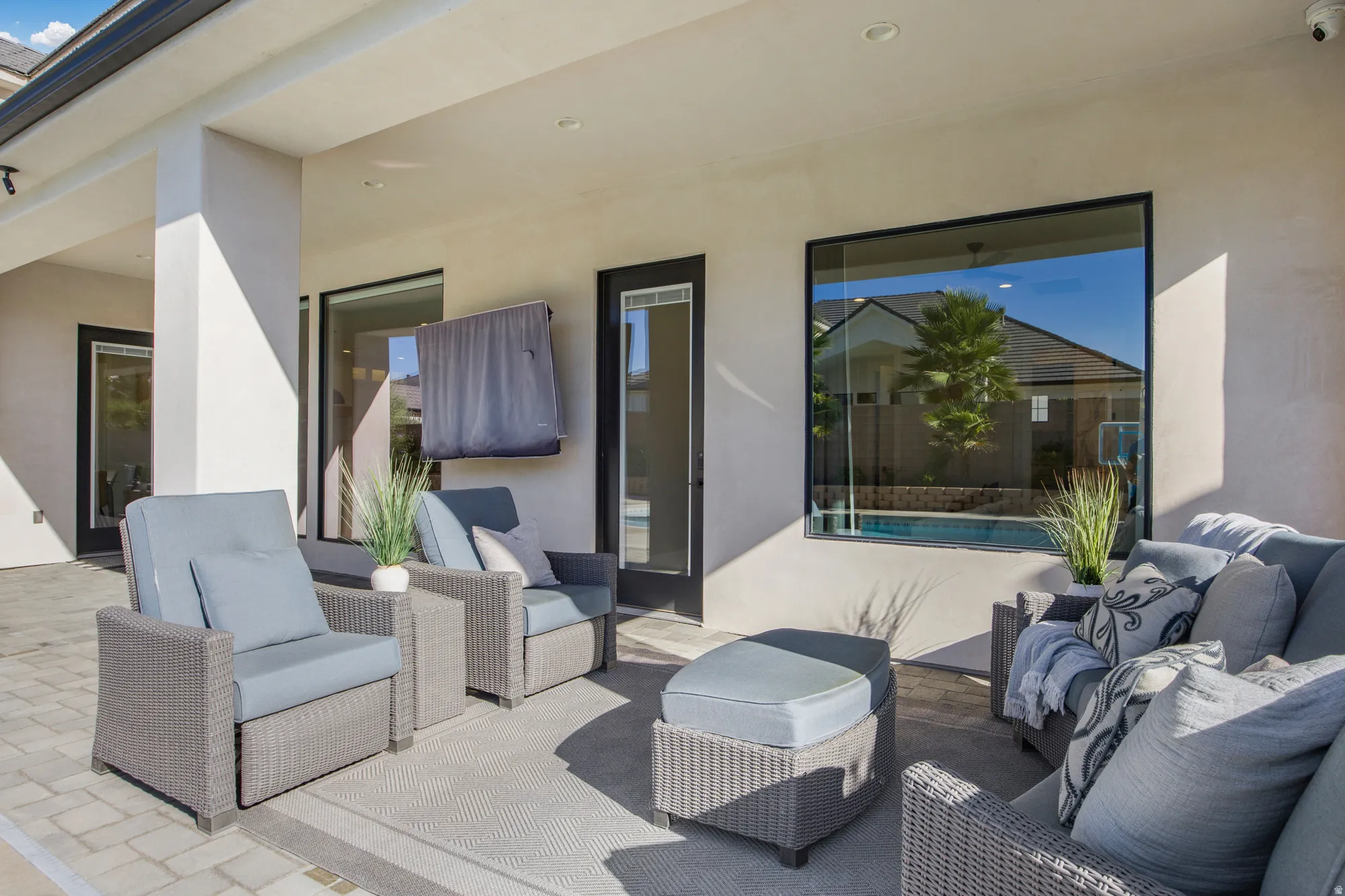 Expansive covered patio featuring recessed lighting, a paver stone surface, large black-framed windows, and direct access to a pool area