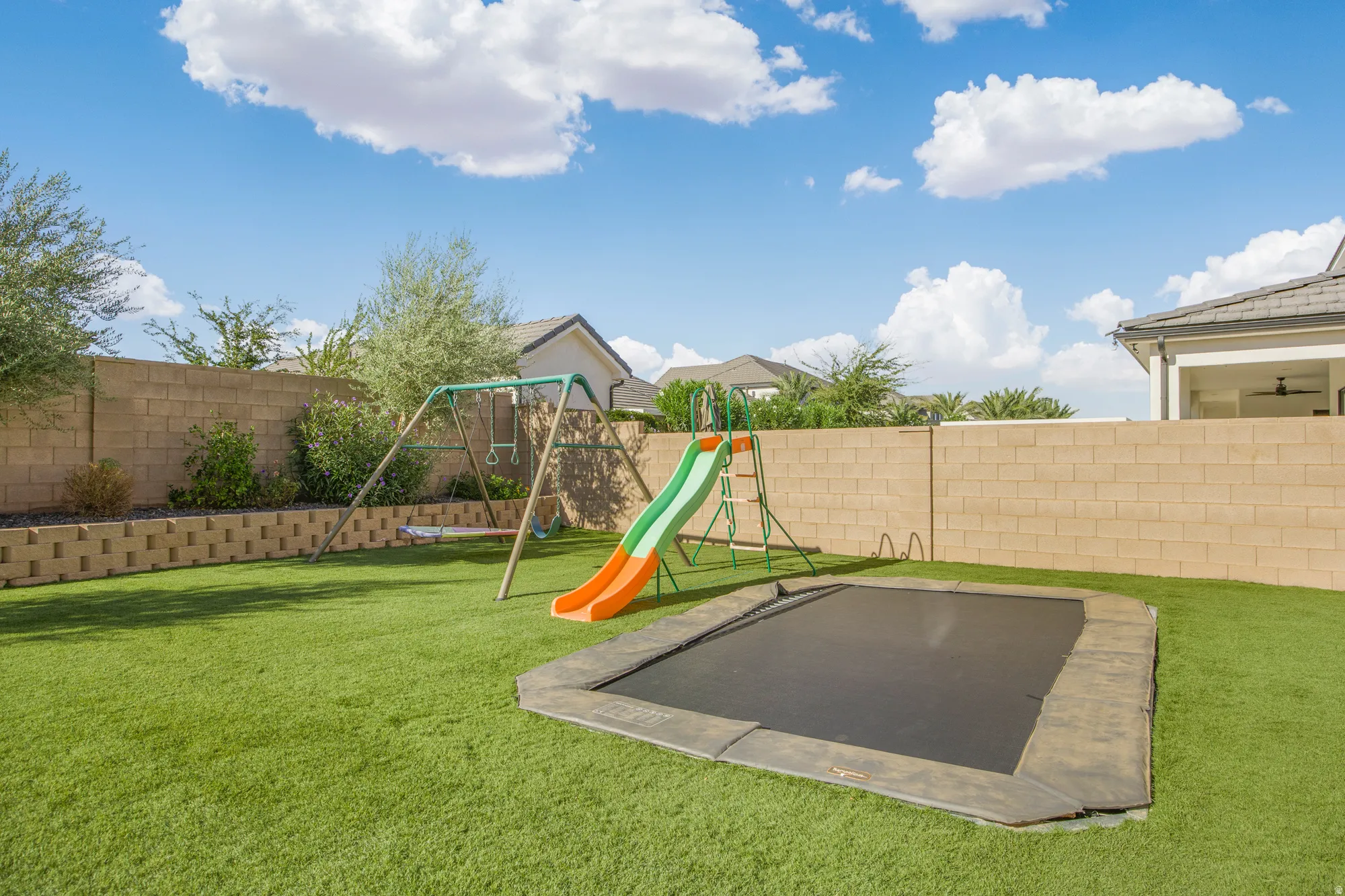 Expansive backyard featuring artificial turf, a block privacy fence, and a tiered retaining wall with integrated landscaping