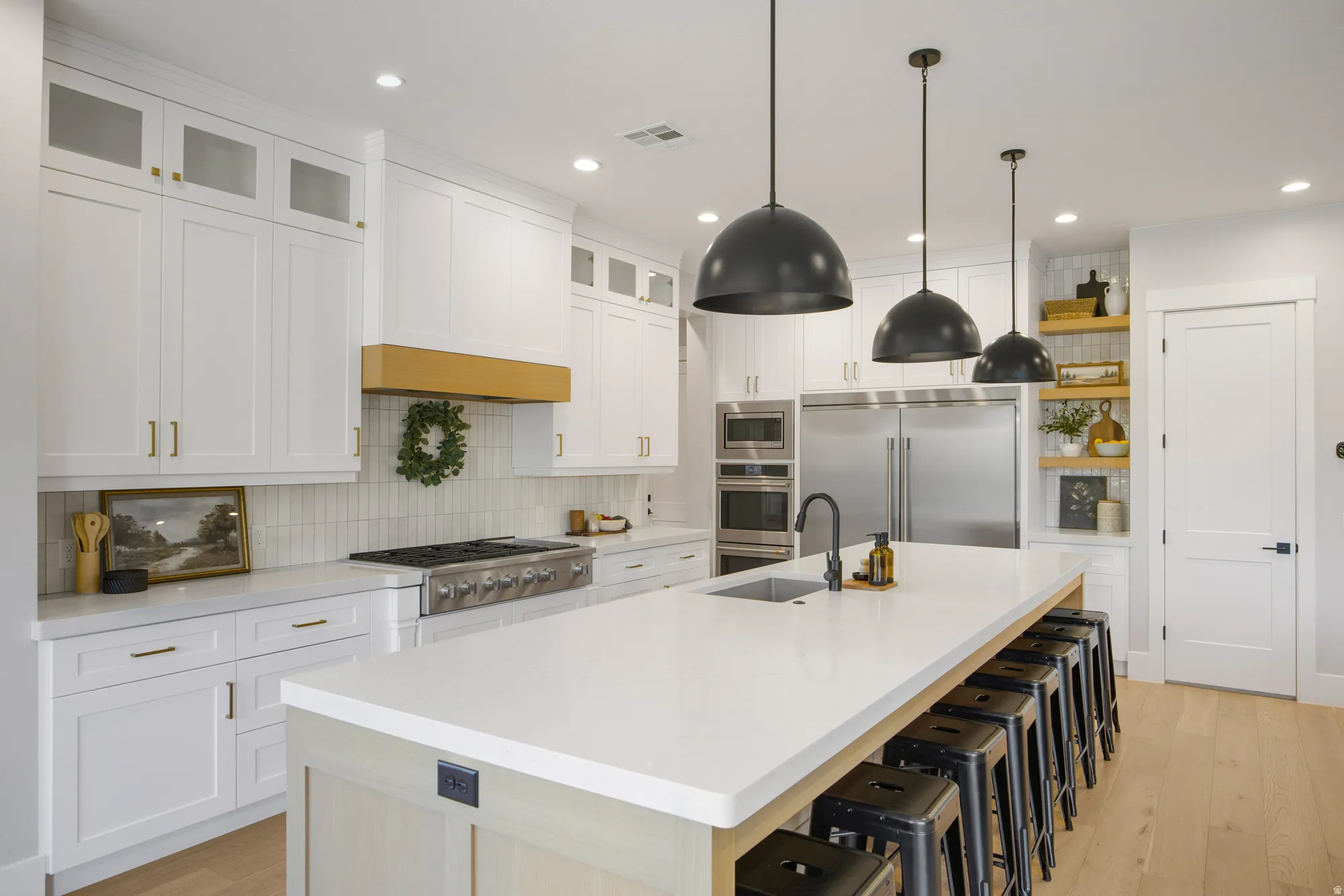Gourmet kitchen with extensive white cabinetry, a large center island, stainless steel appliances, a gas range, and wood-finish flooring