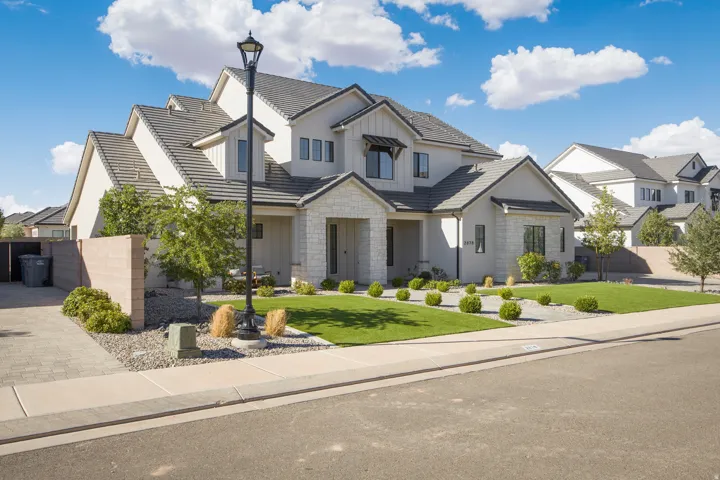 Contemporary exterior featuring a light-colored stucco finish, stone accents, a multi-gabled roofline, a neatly manicured lawn, and a paved driveway
