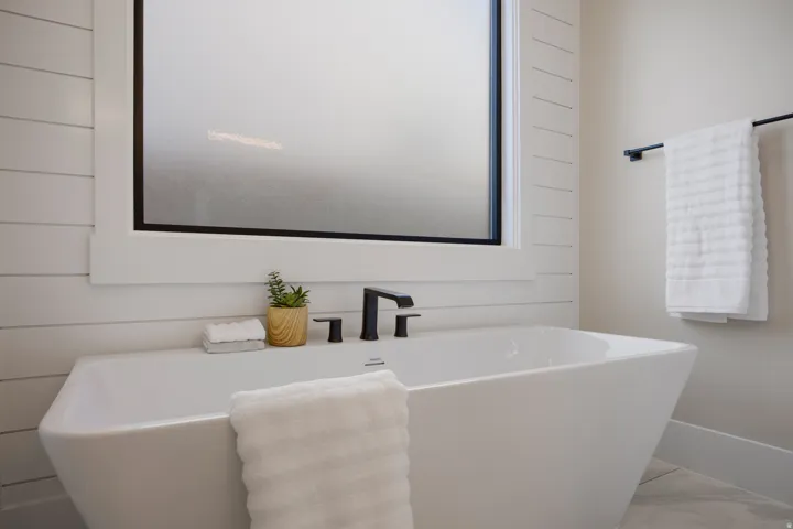 Freestanding soaking tub with matte black fixtures, shiplap accent wall, and a frosted glass window