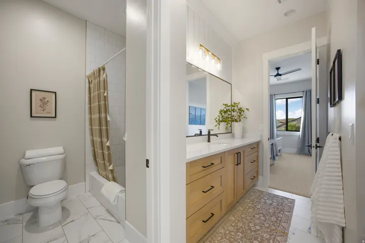 Bathroom featuring a light wood-finish vanity with a quartz countertop, a rectangular undermount sink with a matte black faucet, and a shower with subway tile surround