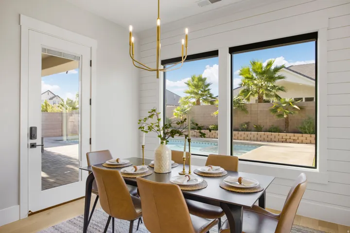 White shiplap accent wall, light wood-finish flooring, gold-tone chandelier, full-light glass door, and large picture windows