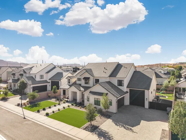 Modern exterior with a light stucco finish, dark roof tiles, an attached multi-car garage, paver driveway, and a landscaped front yard with artificial turf
