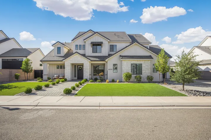 Two-story residence featuring a gray shingle roof, stone and stucco exterior, and a paver driveway