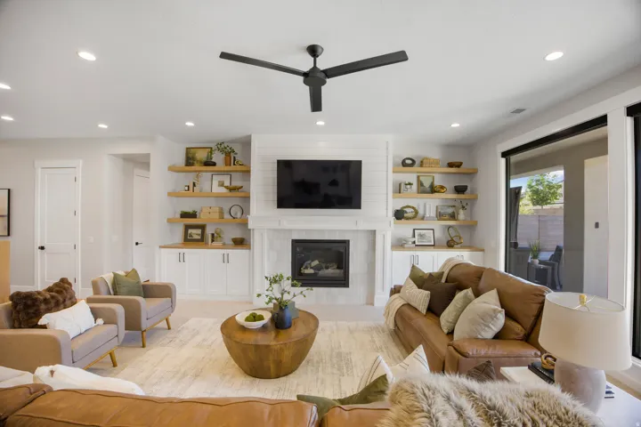 Living area featuring a fireplace, built-in cabinetry, wood-finish floating shelves, recessed lighting, and a ceiling fan